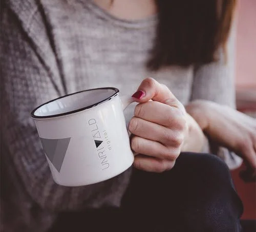 Woman holding a white Unrivald Digital coffee mug in a relaxed workspace